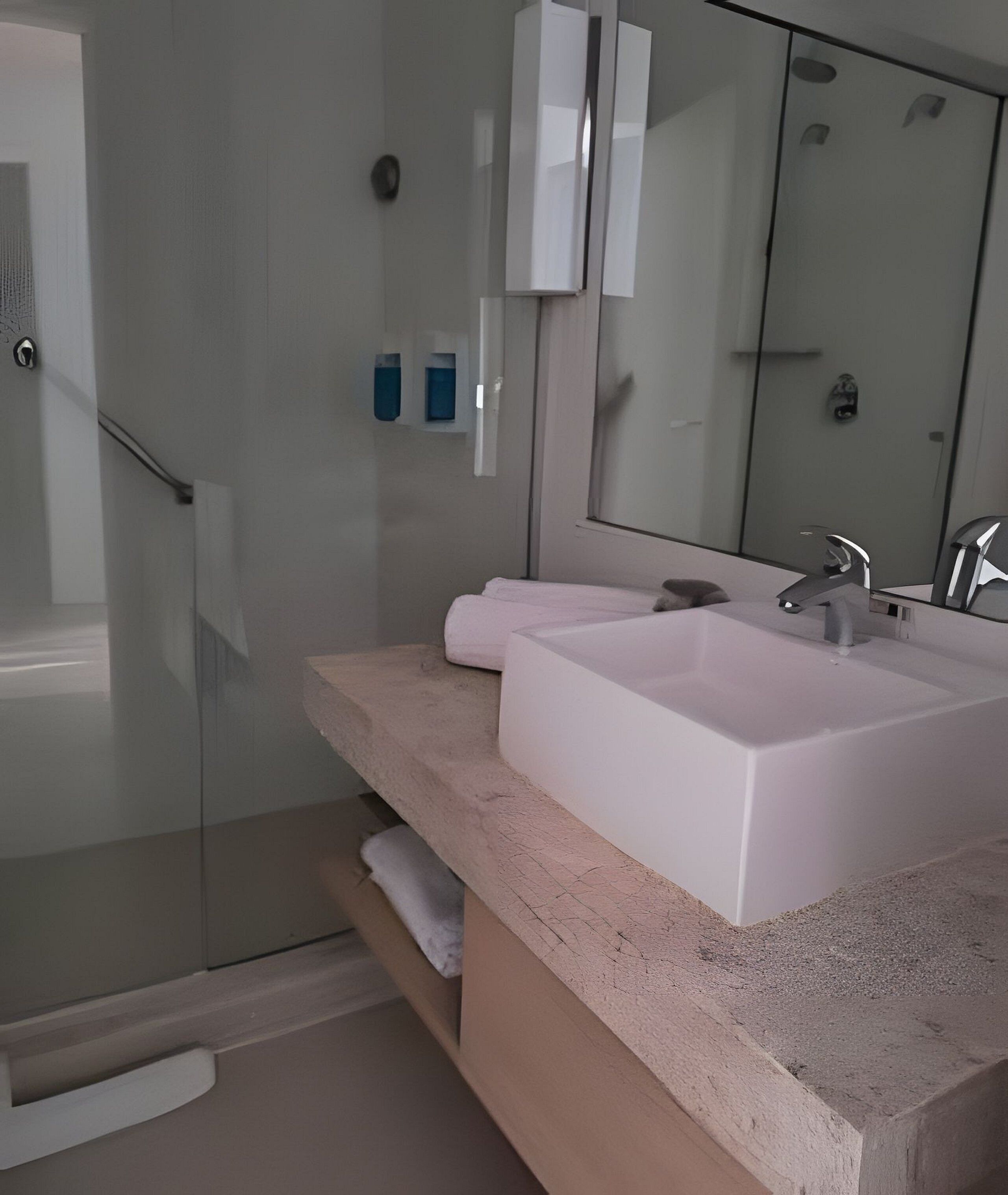 Un baño moderno con cabina de ducha de vidrio, un lavamanos blanco y un espejo grande.