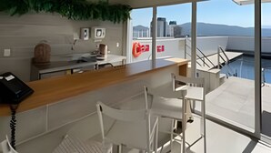 Eine moderne Küche mit Bar, weißen Stühlen und Blick auf die Stadt durch große Fenster.