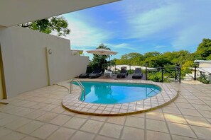 Una piscina con suelo de baldosas, una escalera metálica y sillas de descanso.