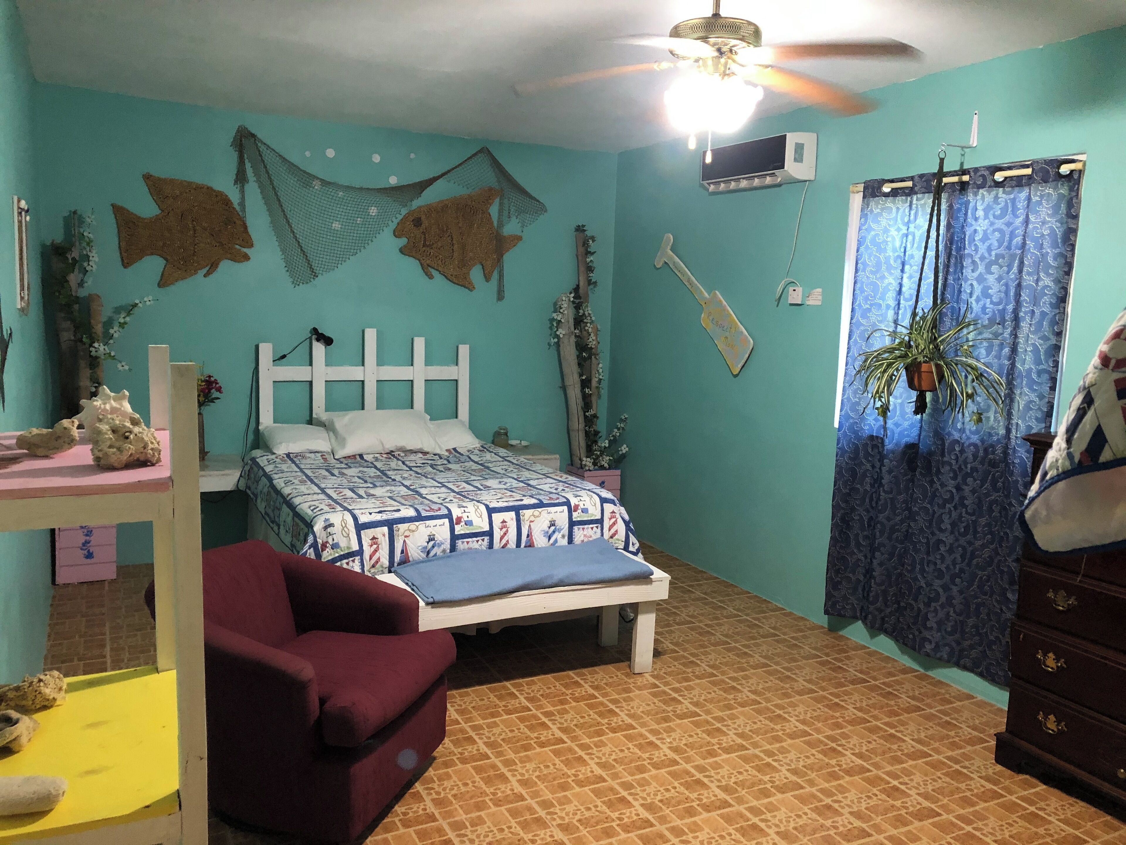 Quarto com cama, escrivaninha, cadeira, cômoda e ventilador de teto.