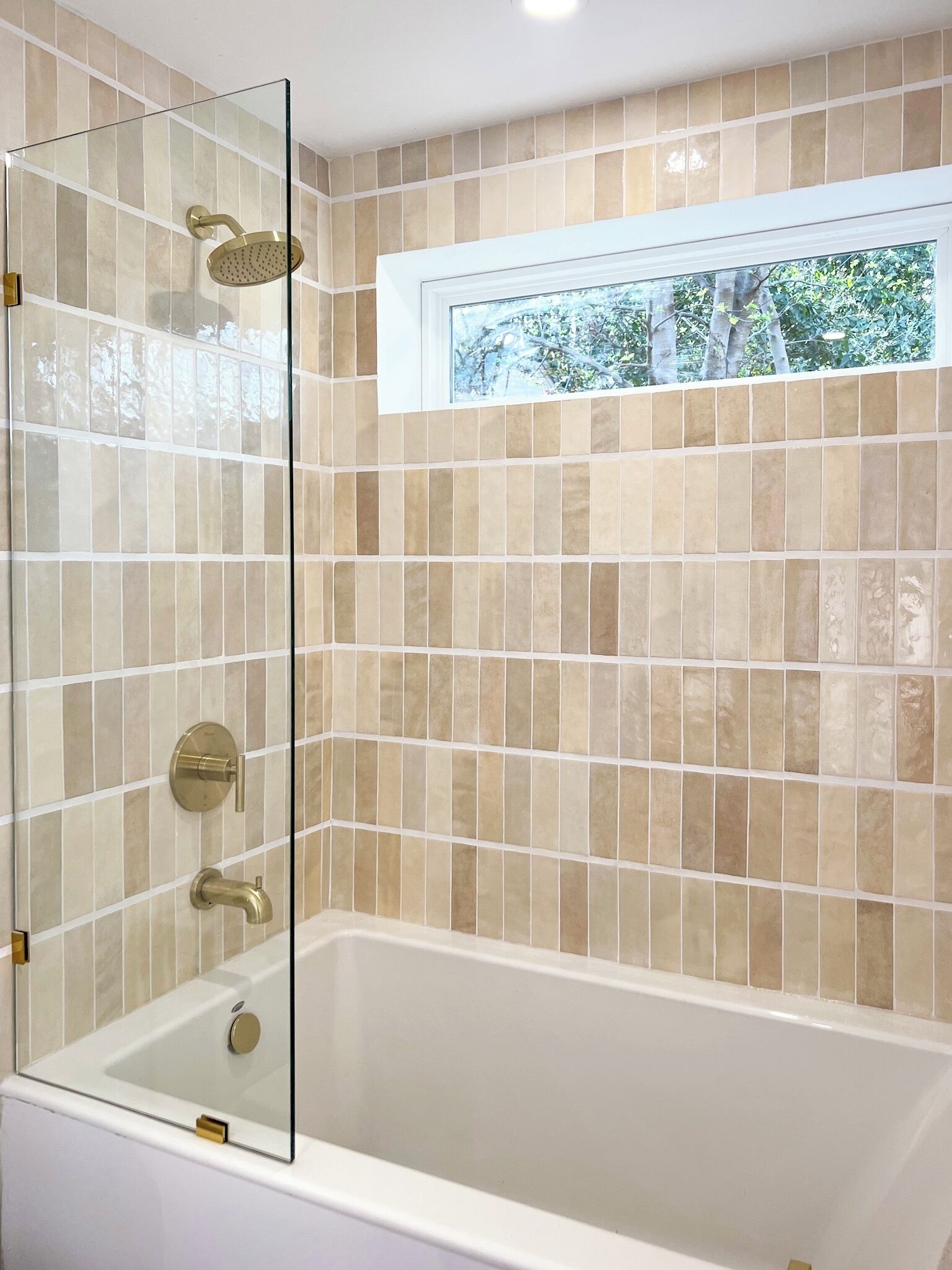 A modern bathroom with a glass-enclosed shower, a bathtub, and a window providing a view of greenery outside.