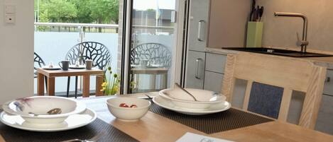 A dining area with a table set for two, a view of the outdoors, and a modern kitchen with a sink and cabinets.