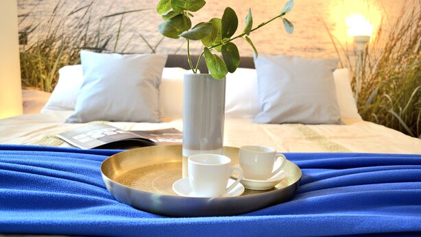 A neatly made bed with white bedding, a tray with two white cups and a bowl, and a potted plant on the bedside table. - KomfortPlus New Construction - Apartment with a sunny balcony and free parking (Bad Zwischenahn)