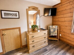 A room with a wooden dresser, a mirror, a television mounted on the wall, and a small shelf with a patterned cloth. - Cozy farmhouse cabin, pet friendly (Branson)