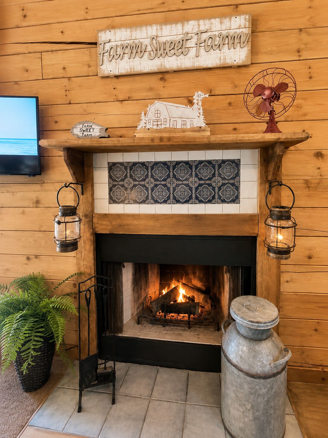 A fireplace with a farm-themed sign above, a decorative house model, and a fan on the mantel.