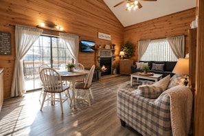 A cozy cabin interior with a dining area, fireplace, sofa, and a television. - Cozy farmhouse cabin, pet friendly (Branson)