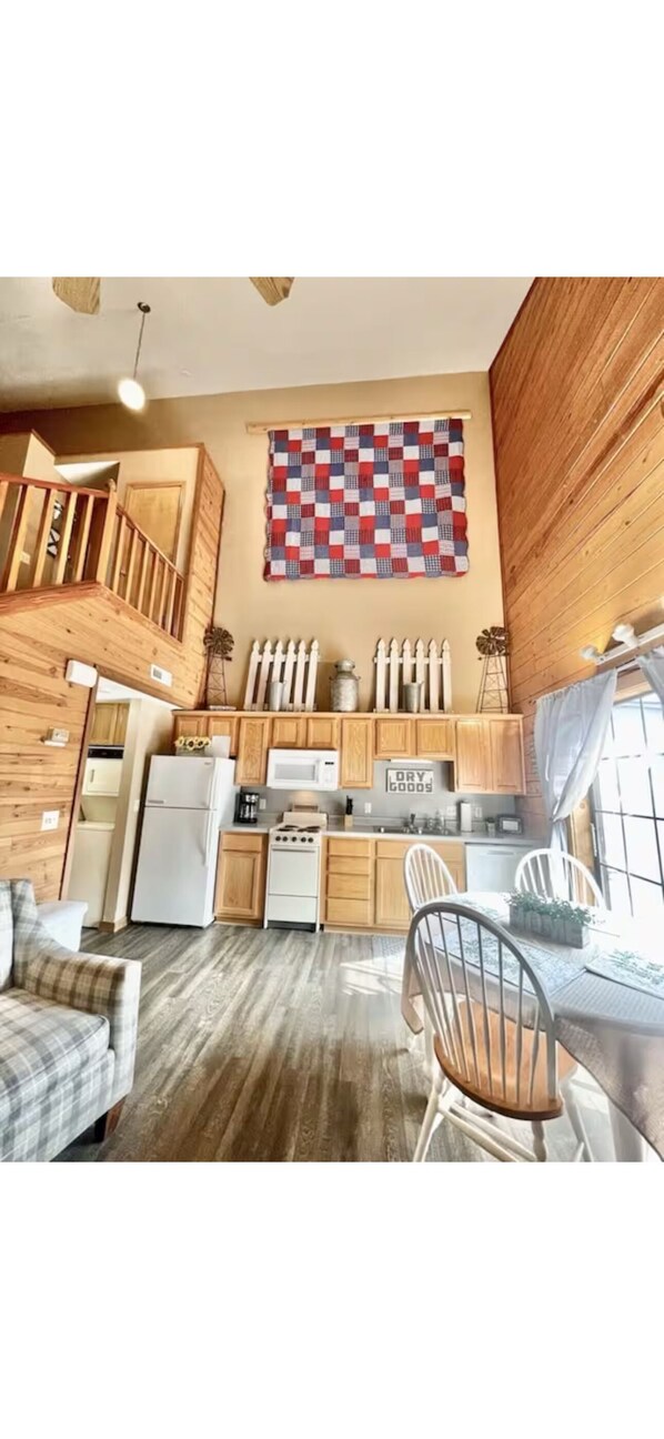 A compact kitchen with wooden cabinets, a dining area with a table and chairs, and a staircase leading to an upper level.