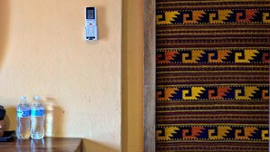 A room with a wall-mounted thermostat, two water bottles on a wooden table, and a patterned tapestry. - Mountain view room (Oaxaca)