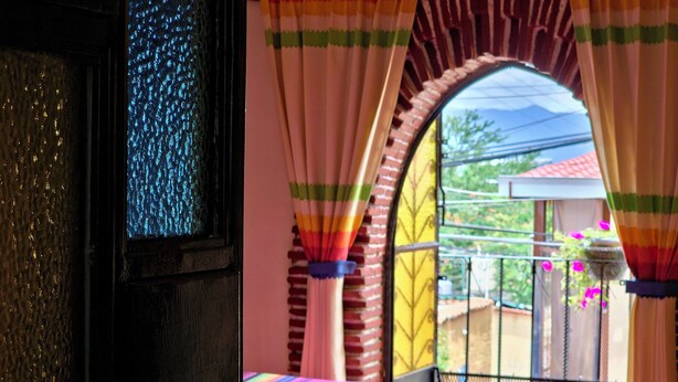 A room with a bed, a window with curtains, and a balcony with a railing. - Mountain view room (Oaxaca)