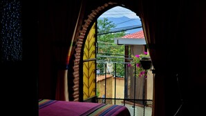A room with a bed, a window with a view of buildings, and a balcony with a railing. - Mountain view room (Oaxaca)