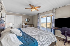 Une chambre d’hôtel équipée d’un lit, d’un bureau, d’une chaise, d’un ventilateur de plafond, d’une télévision et offrant une vue sur la plage.
