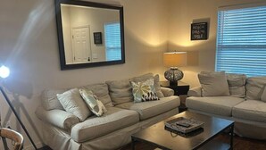 A living room with a beige sectional sofa, a coffee table, a floor lamp, and a wall-mounted mirror. - Cozy home Gated community special deals (Kissimmee)