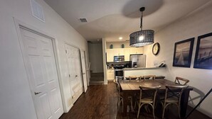 A modern kitchen with white cabinets, a stainless steel refrigerator, and a dining area with a wooden table and chairs. - Cozy home Gated community special deals (Kissimmee)
