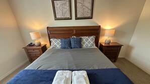 A neatly made bed with a blue blanket, two white towels, and patterned pillows. There are two bedside tables with lamps and a framed map on the wall. - Cozy home Gated community special deals (Kissimmee)