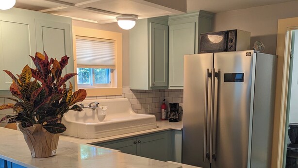 A modern kitchen with a central island, stainless steel appliances, and light green cabinetry.