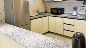 Una cocina compacta con un refrigerador de acero inoxidable, un microondas, un lavamanos y una encimera de granito.