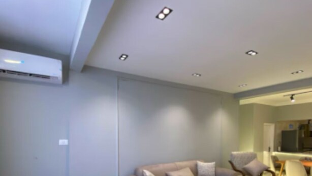 Una sala de estar moderna con un sofá color beige, un cojín estampado, una mesa de centro de madera e iluminación empotrada en el techo.