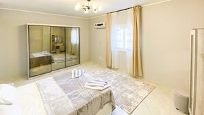 Un dormitorio con cama, un espejo grande, un armario, una ventana con cortinas y una lámpara en el techo.