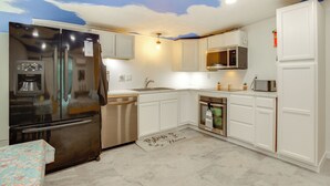 Una cucina moderna con mobili bianchi, elettrodomestici in acciaio inossidabile e un affresco a tema nuvole sul soffitto.