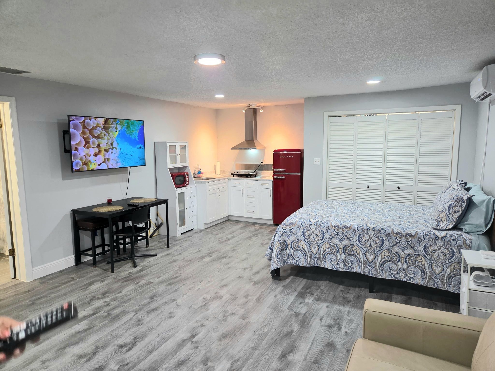 A compact room with a bed, a desk, a TV, a microwave, and a red refrigerator.