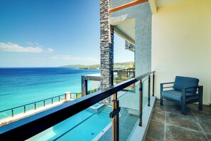 A balcony with a glass railing overlooking a swimming pool and the ocean. - Luxury Oceanfront Villa Fully Staffed (Tower Isle)