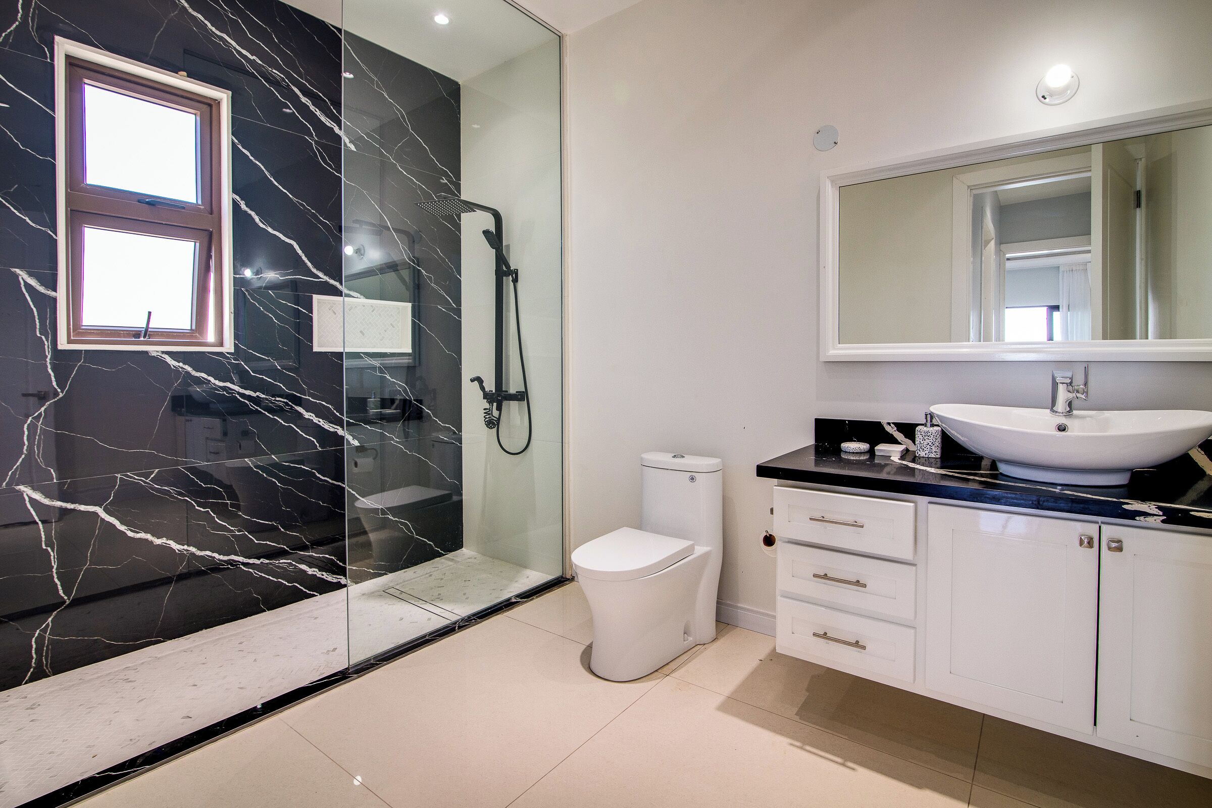 Un baño moderno con cabina de ducha de vidrio, inodoro blanco, un lavabo grande con espejo y un salpicadero de mármol.