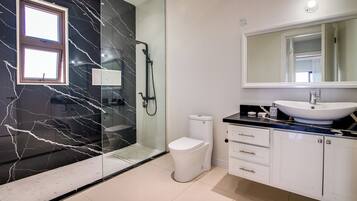 Un baño moderno con cabina de ducha de vidrio, inodoro blanco, un lavabo grande con espejo y un salpicadero de mármol.