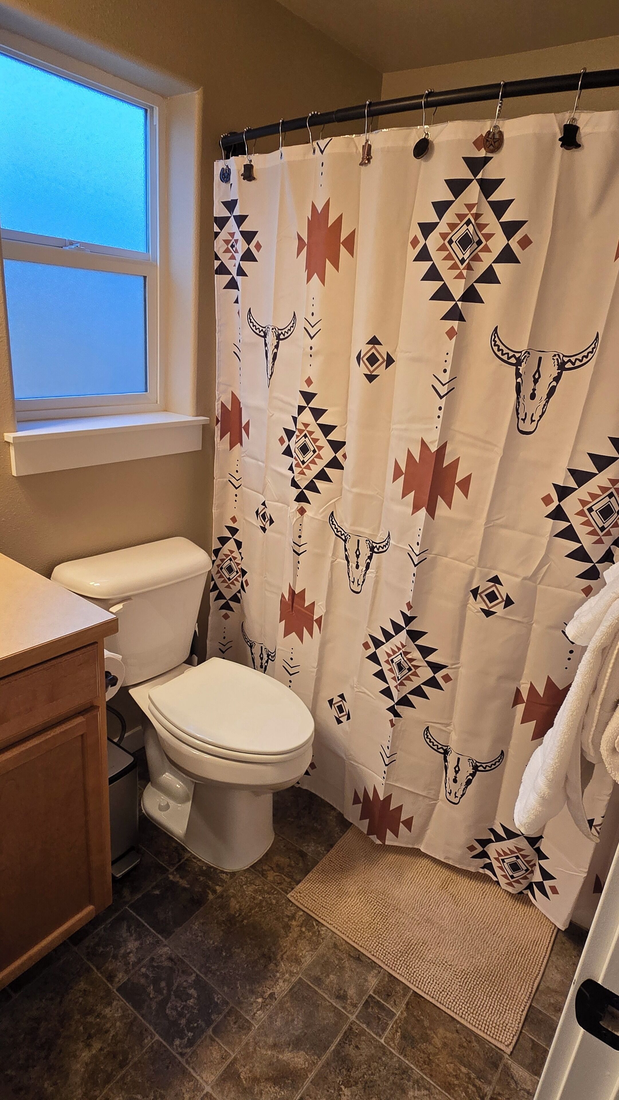 Une salle de bain équipée d’un rideau de douche orné de motifs géométriques, de toilettes, d’un lavabo et d’une fenêtre.