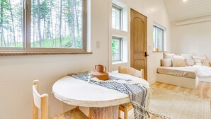 A cozy room with a round table, chairs, a bed, and large windows offering a forest view. - Romantic Forest Cabin by Flathead Lake (Polson)