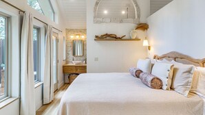 A bedroom with a large bed, a wooden headboard, a stone wall arch, a mirror, a shelf with decorative items, and a window with curtains. - Romantic Forest Cabin by Flathead Lake (Polson)