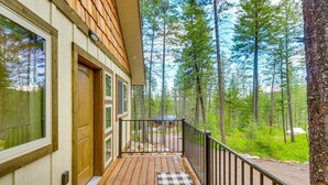 A wooden deck with a checkered mat, a black metal railing, and a view of a forested area. - Romantic Forest Cabin by Flathead Lake (Polson)