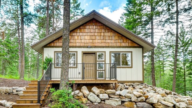 A cabin with a stone foundation, wooden exterior, and a porch with steps leading to a door. - Romantic Forest Cabin by Flathead Lake (Polson)