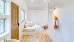 A modern bedroom with a large bed, a wooden door, and a small shelf with decorative items. - Romantic Forest Cabin by Flathead Lake (Polson)