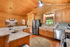 A wooden cabin interior with a kitchen featuring granite countertops, stainless steel appliances, and wooden cabinets.