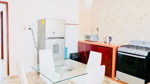 Una cucina compatta con frigorifero, microonde, bollitore, fornello e un tavolo in vetro con sedie.