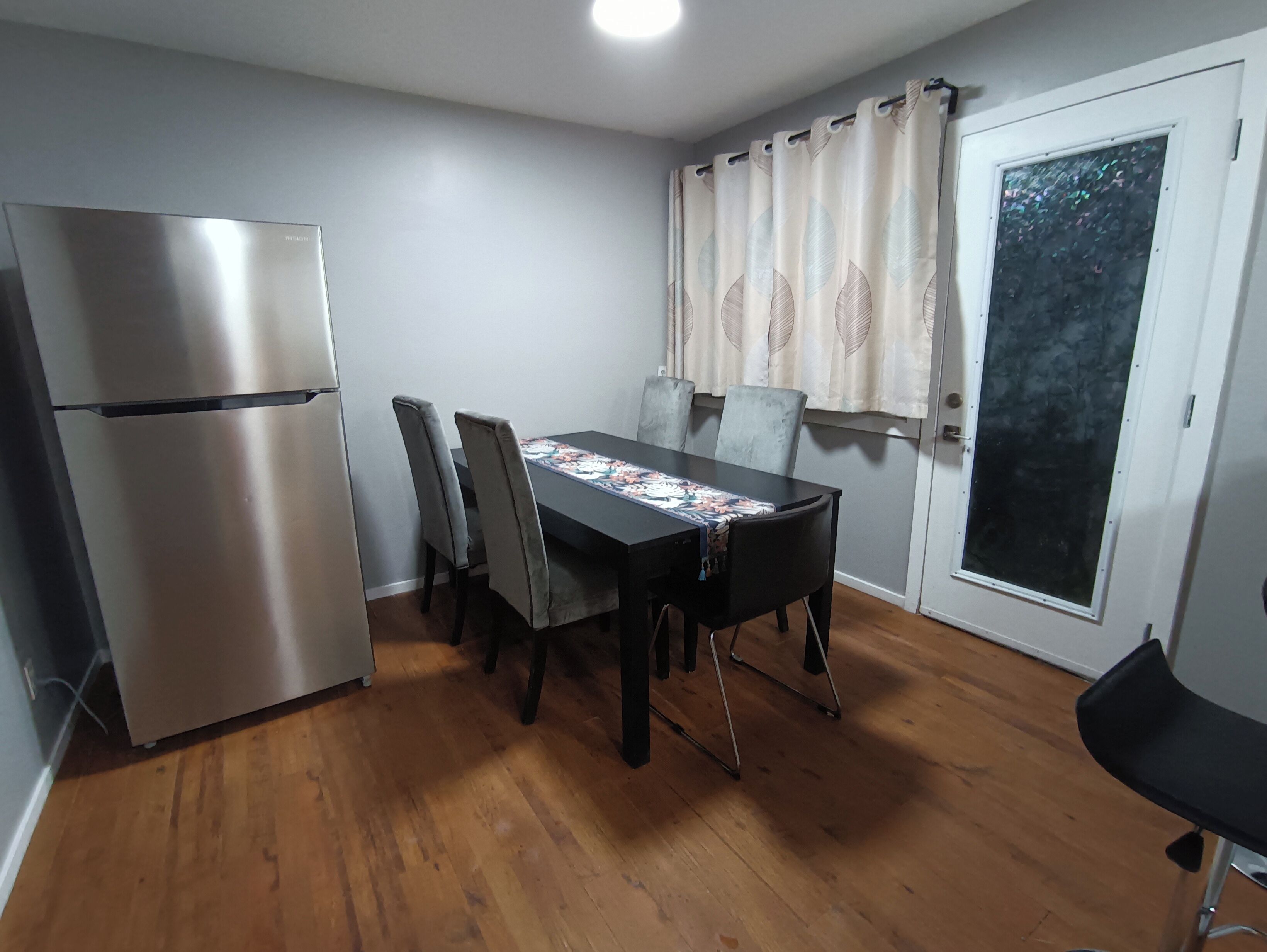 A compact kitchen with a refrigerator, dining table, chairs, and a window with curtains.