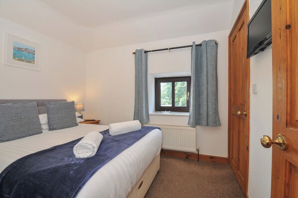 Un dormitorio con cama, ventana con cortinas, radiador, puerta de madera y un cuadro enmarcado en la pared.