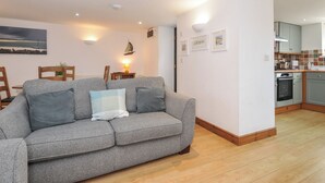 Ein modernes Wohnzimmer mit grauem Sofa, Holzboden und einer Küchenzeile mit grauen Schränken und einer gefliesten Spritzschutzwand.