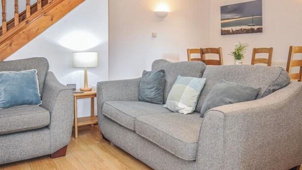 Ein Wohnzimmer mit grauem Sofa, einer Holztreppe, einer Wandlampe und einem gerahmten Bild.