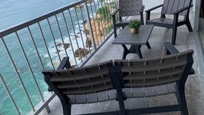 Un balcón con vista al océano, que incluye dos sillas de madera y una mesa con una planta en maceta.