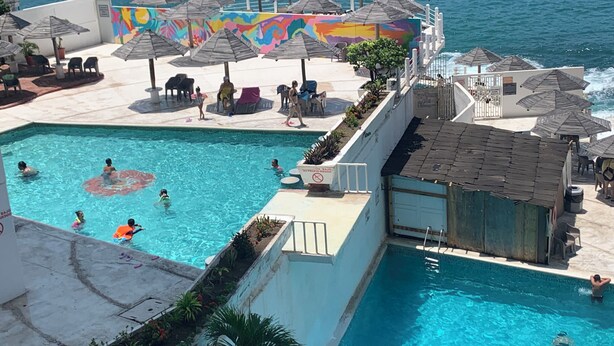 Zona de piscina con múltiples sombrillas, un mural y vista al mar.