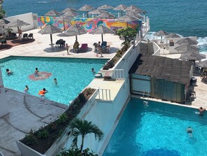 A pool area with multiple umbrellas, a mural, and a view of the sea. - Enjoyable Suite front beach in Acapulco de Juárez (Acapulco de Juárez)