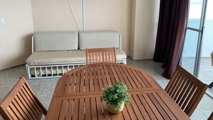 Una habitación con una mesa redonda de madera, cuatro sillas de madera, un sofá color beige y un televisor colocado en la pared.