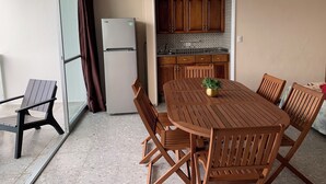 Una cocina compacta con armarios de madera y horno empotrado, un comedor con mesa redonda y sillas, y un puerta corrediza de vidrio que da a un balcón.