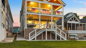 A two-story building with a covered porch, a flag, and a staircase leading to the entrance. - Barefoot Dreams Waterfront w/Flat Lot, Pool, Paddleboards (Winchester)