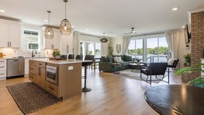 A modern kitchen with a central island, dining area with a sofa and chairs, and a large window providing natural light. - Barefoot Dreams Waterfront w/Flat Lot, Pool, Paddleboards (Winchester)