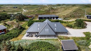 Een modern huis met een schuin dak, omgeven door een aangelegde tuin met zitplaatsen.