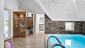 Een modern binnenzwembad met een stenen muur en een houten sauna.