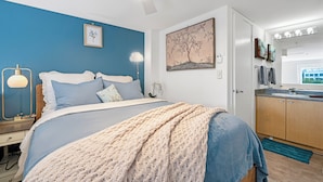 Quarto com cama, mesa de cabeceira, luminária e obra de arte na parede.