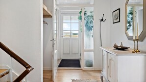 Un couloir avec un escalier en bois, une porte blanche donnant sur un beau paysage, un miroir et une petite table avec des bougies.